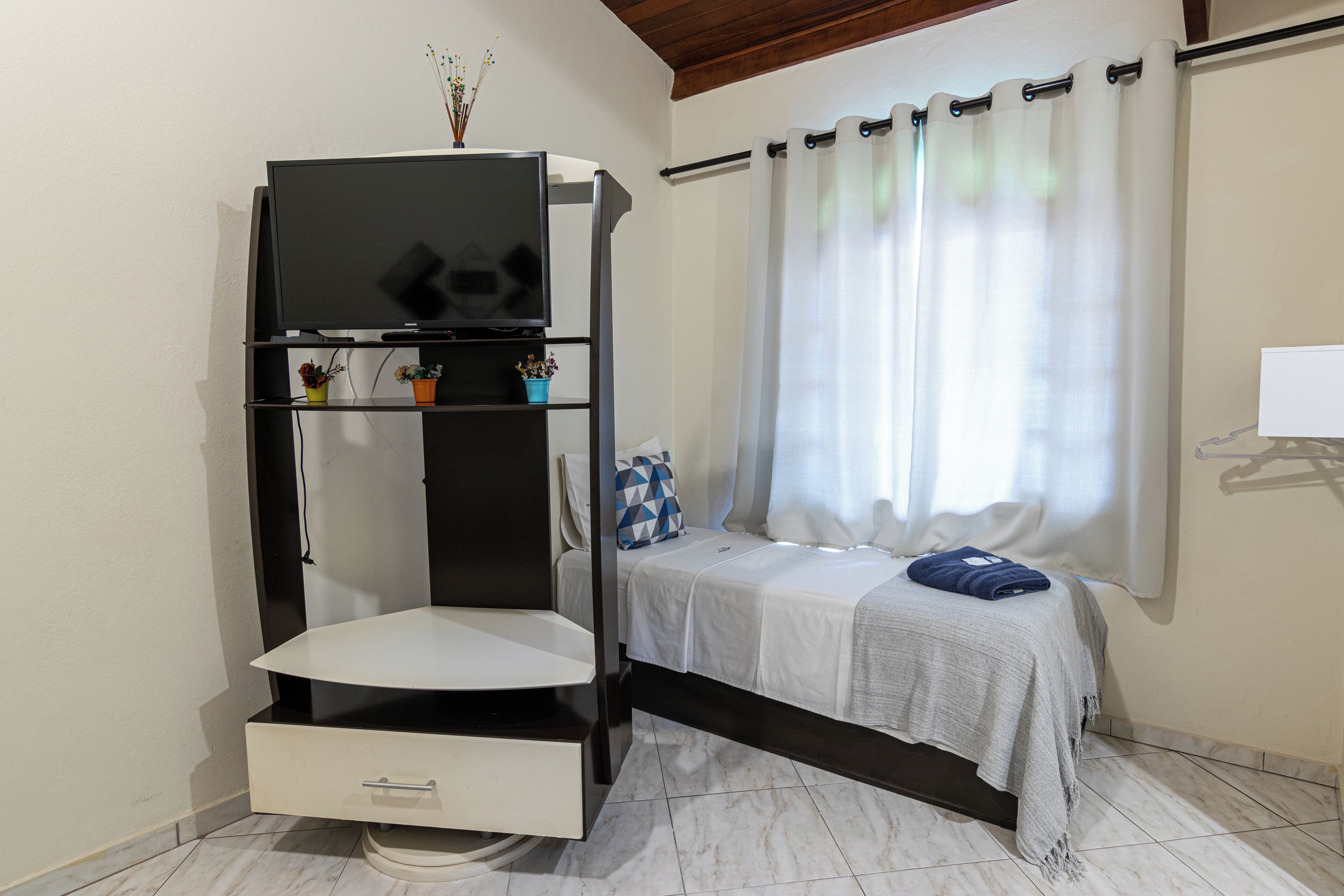 Una camera da letto con un letto, una televisione su uno scaffale, un tavolino e una finestra con tende.