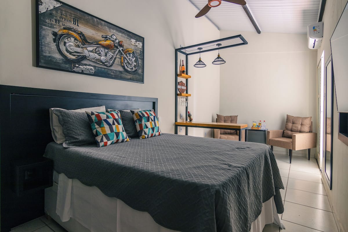 Ein Schlafzimmer mit einem Bett, einem Schreibtisch, zwei Stühlen, einem Motorradbild und einem Deckenventilator.