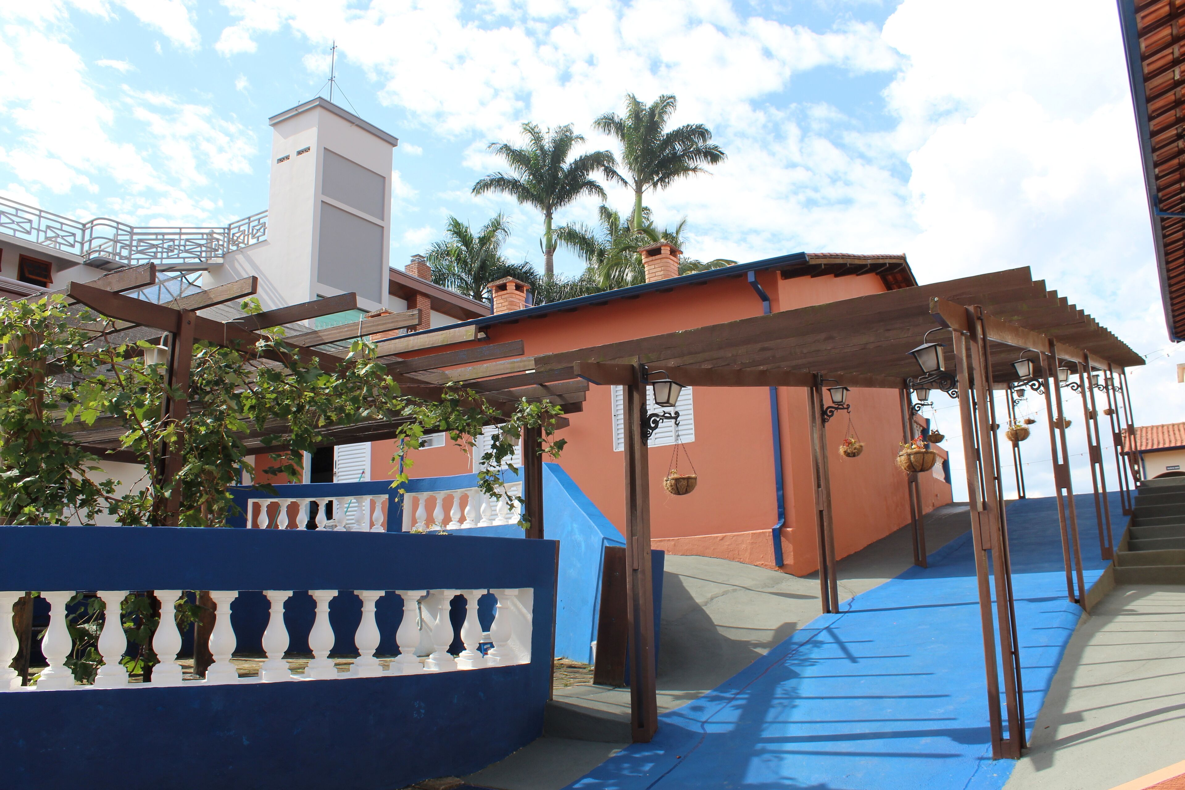 Un espace extérieur aux couleurs bleu et blanc, agrémenté d’une pergola, d’un escalier et d’un bâtiment à la façade rouge.