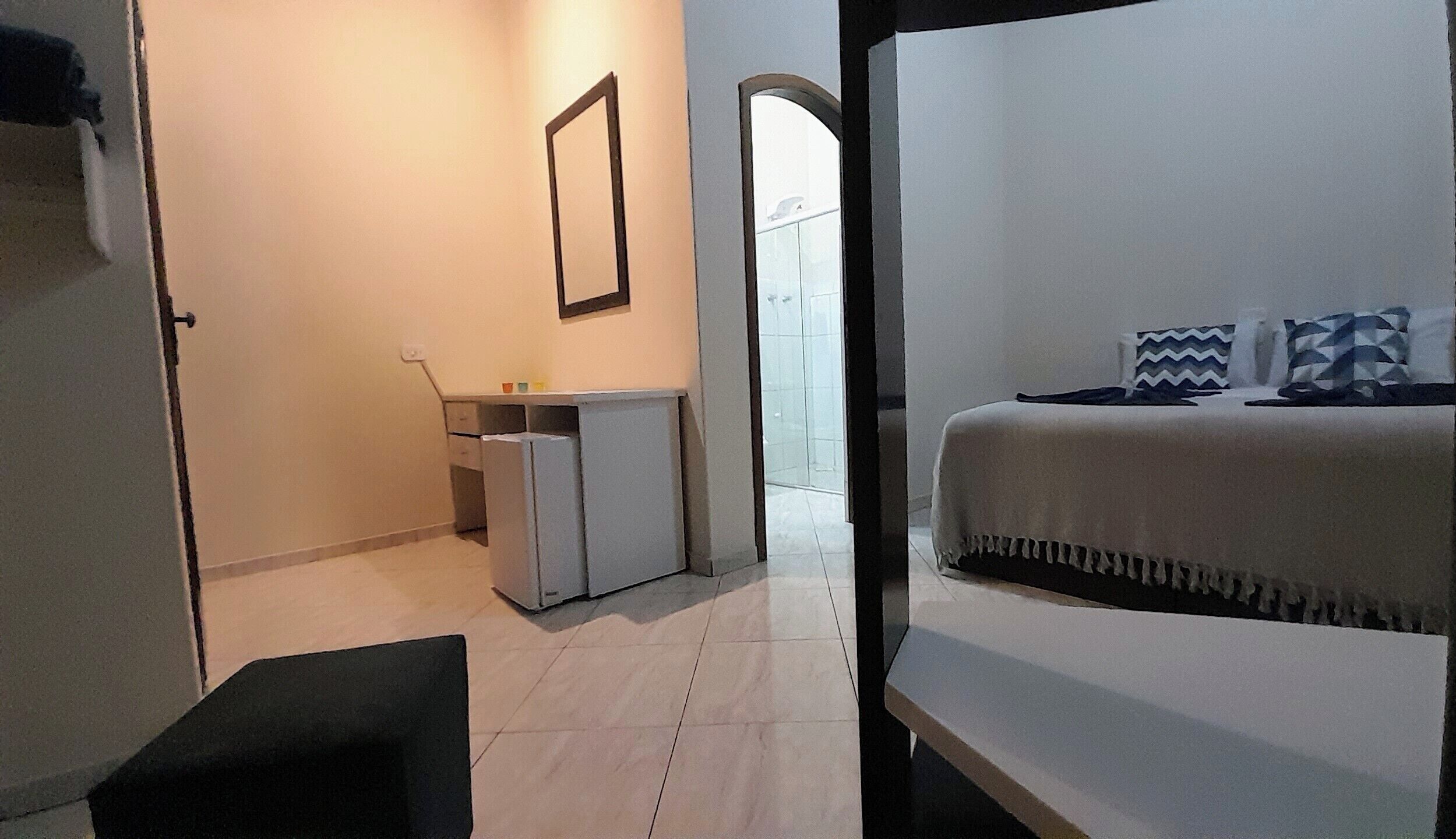 Une chambre d’hôtel avec un lit, un petit bureau, un miroir et une porte donnant sur une salle de bain.