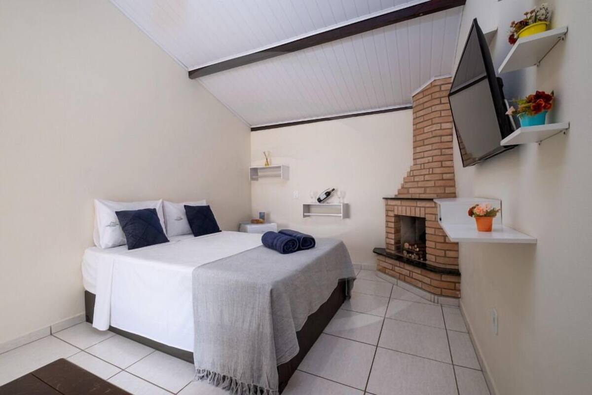 Ein Schlafzimmer mit einem Bett, einem an der Wand montierten Fernseher, einem Kamin und einer kleinen Ablage mit Blumen.