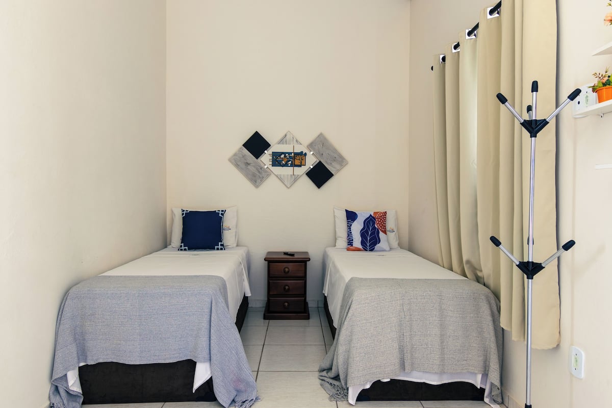 Ein Hotelzimmer mit zwei Betten, einem kleinen Nachttisch, einem an der Wand befestigten Kleiderhaken und einem Wandbild.