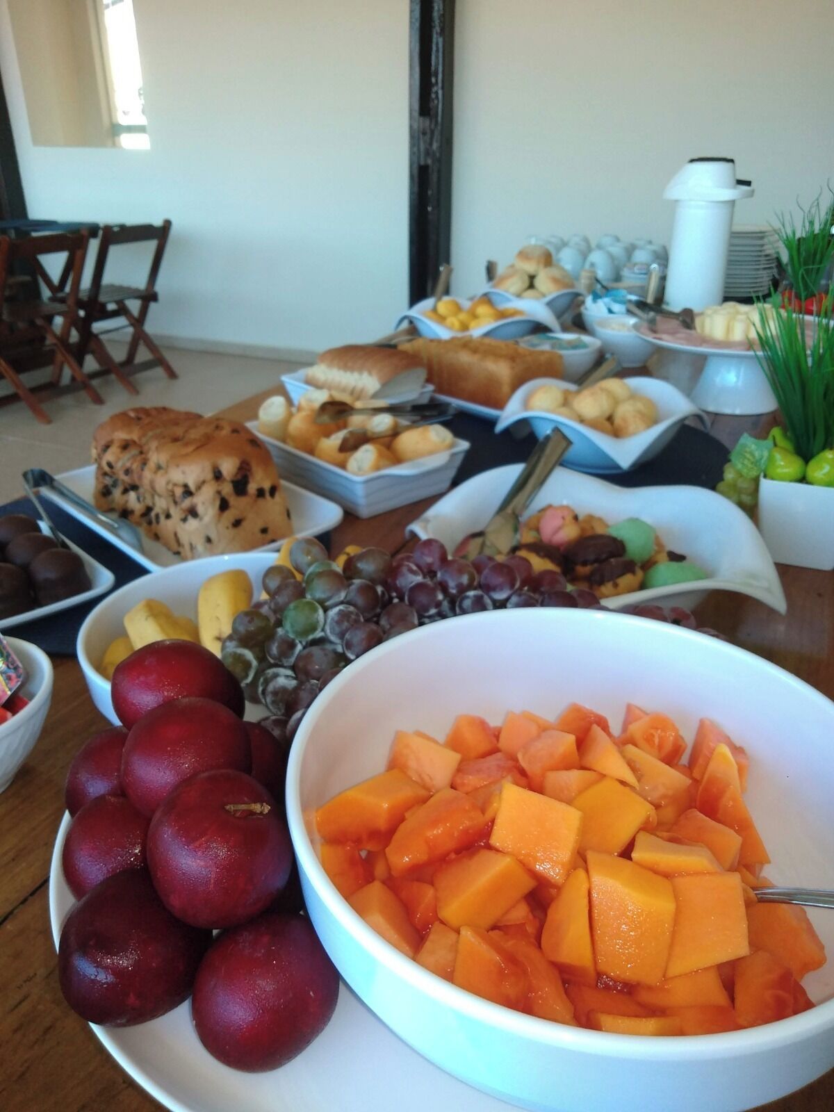 A buffet table with various food items including fruits, pastries, and bread.