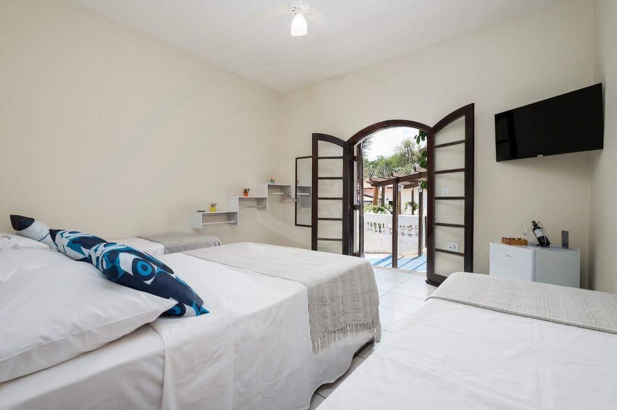 A hotel room with two beds, a TV mounted on the wall, and a view of the outdoor area through an open door.