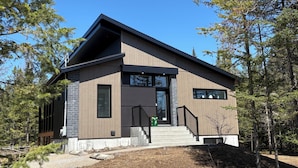 A modern two-story house with a prominent entrance, large windows, and a staircase leading to the main door.