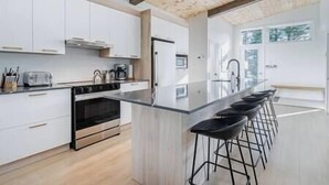 A modern kitchen with white cabinets, a central island with bar stools, and a built-in oven.