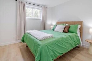 Ein ordentlich bezogenes Bett mit grüner Bettwäsche und weißer Tagesdecke, ein hölzerner Kopfteil und ein Fenster mit Vorhängen.