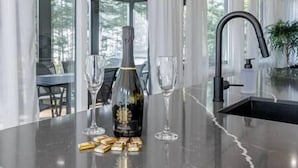 A kitchen counter with a bottle, glasses, and food items.