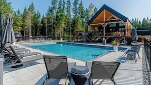 A swimming pool with lounge chairs and a wooden cabin in the background.