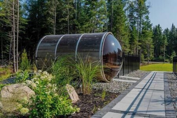 A cylindrical structure with a reflective surface, surrounded by a landscaped garden with rocks and plants, and a paved walkway.