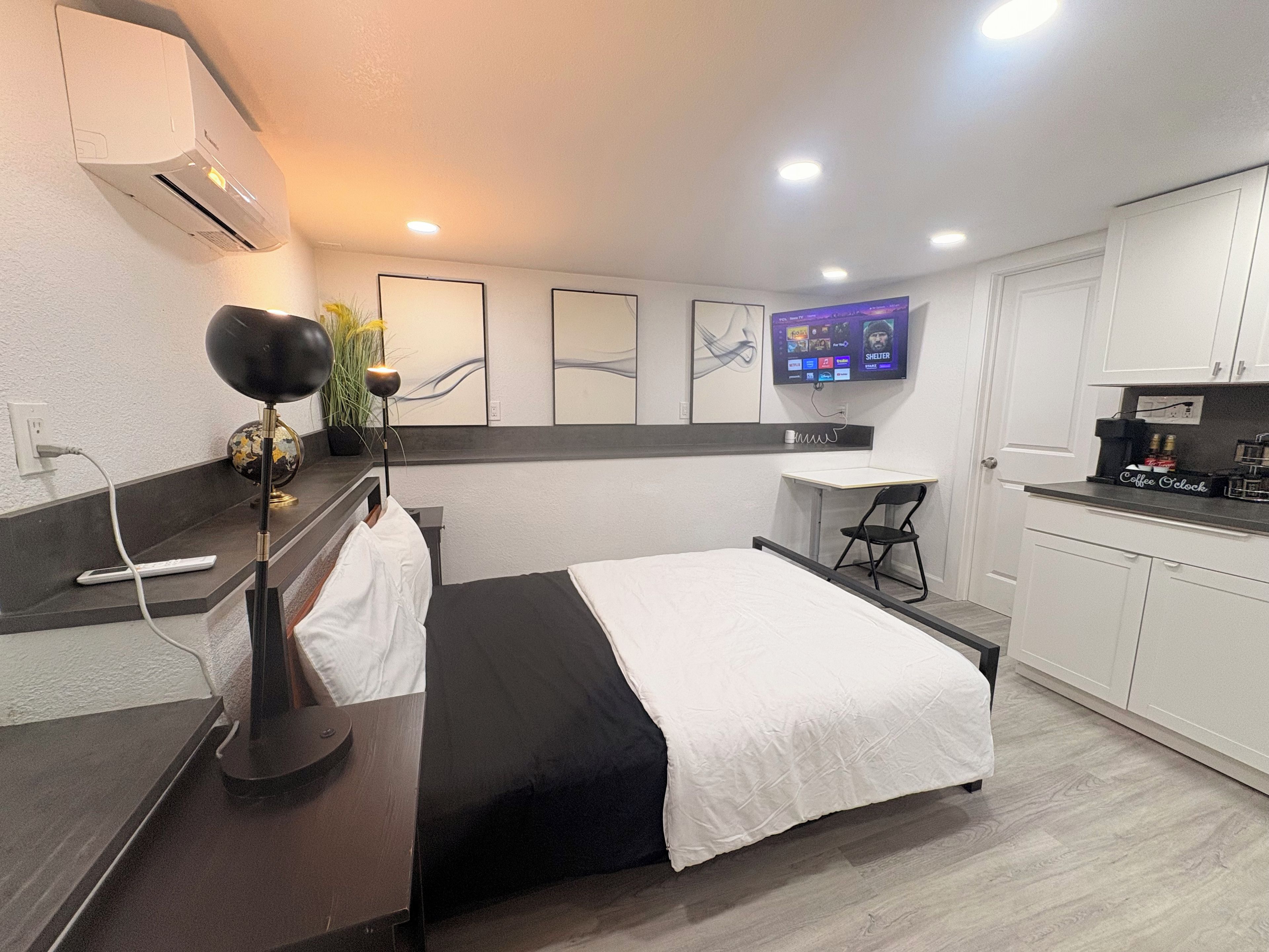 A modern hotel room with a bed, desk, and kitchenette.