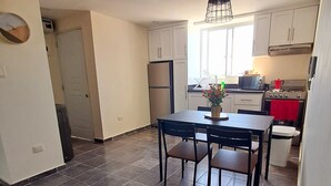 Una cocina moderna con armarios blancos, una mesa de comedor con sillas, una lámpara colgante y un ventanal con vistas.