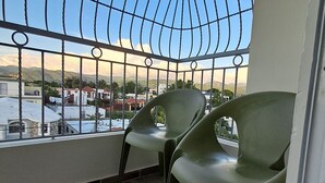 Un balcón con barandilla de metal y dos sillas de plástico verde.