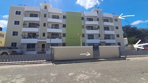 Un edificio residencial de varios pisos con balcones, una entrada protegida por un portón y un cielo despejado.