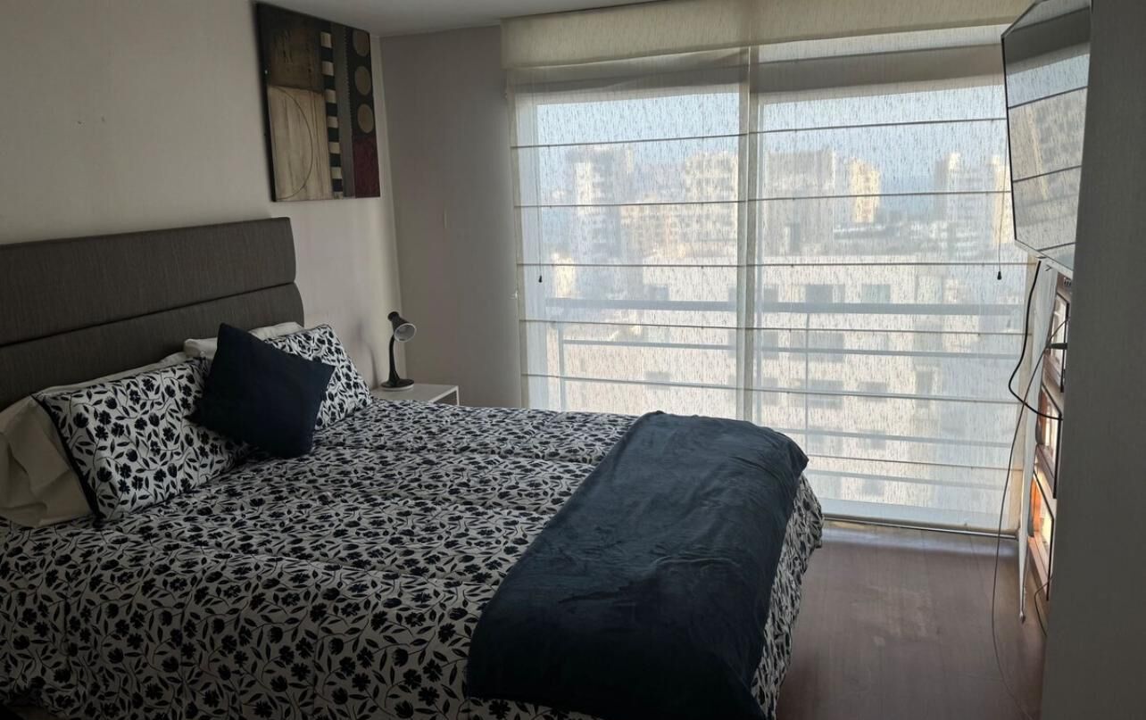 A bedroom with a bed, a nightstand, a lamp, and a window with blinds.