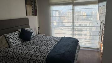 A bedroom with a bed, a nightstand, a lamp, and a window with blinds.