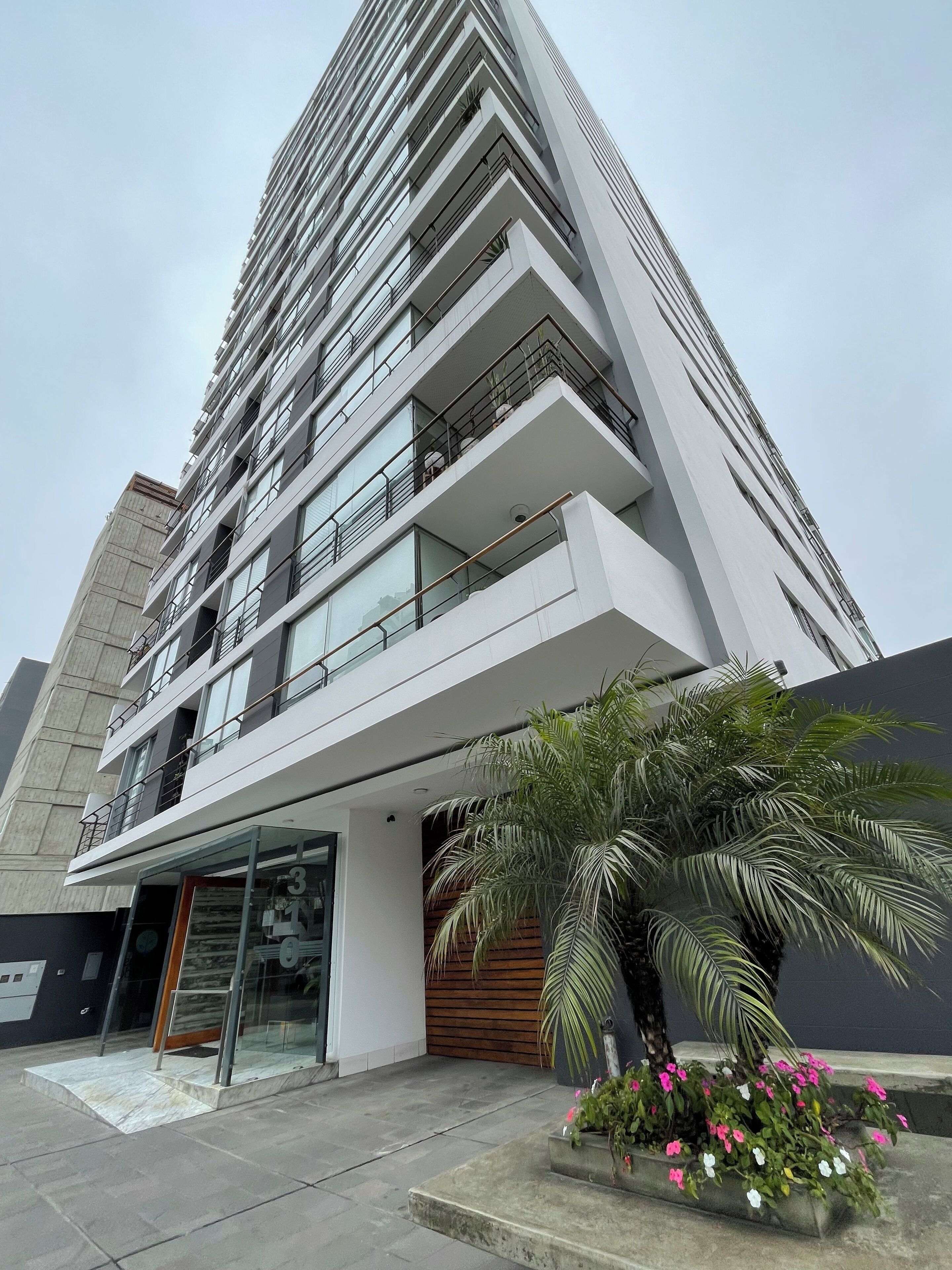 A modern high-rise building with multiple balconies, large windows, and a glass entrance.
