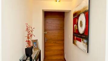 A hallway with a wooden door, a glass table with a vase and picture frame, and a large abstract painting on the wall.