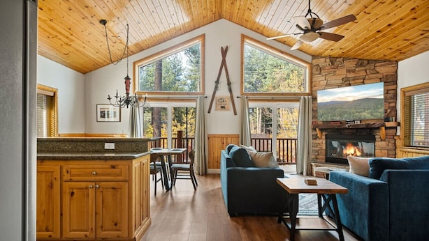 A spacious living area with a fireplace, wooden ceiling, and large windows.