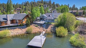 Un chalet au bord du lac, doté d’une jetée qui s’avance sur l’eau, entouré d’une forêt dense et d’autres bâtiments résidentiels.