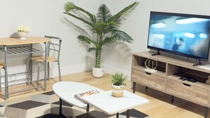 Ein modernes Wohnzimmer mit Essbereich, einer großen Topfpflanze, einem Flachbildfernseher und einem Gemälde an der Wand.