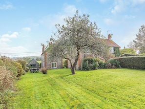 A stone house with a green roof, surrounded by a well-maintained lawn and a large tree.