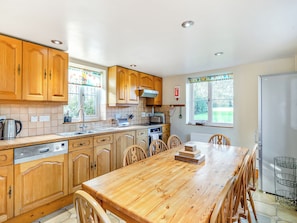 A kitchen with wooden cabinets, a stainless steel dishwasher, a built-in oven, and a dining area with a wooden table and chairs.