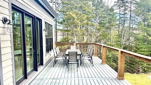 Terraza de madera con mesa y sillas, con vista a un área boscosa.