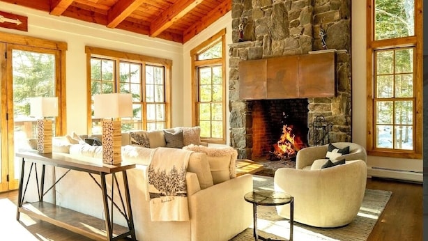 Una sala de estar acogedora con chimenea de piedra, vigas de madera y ventanas amplias.