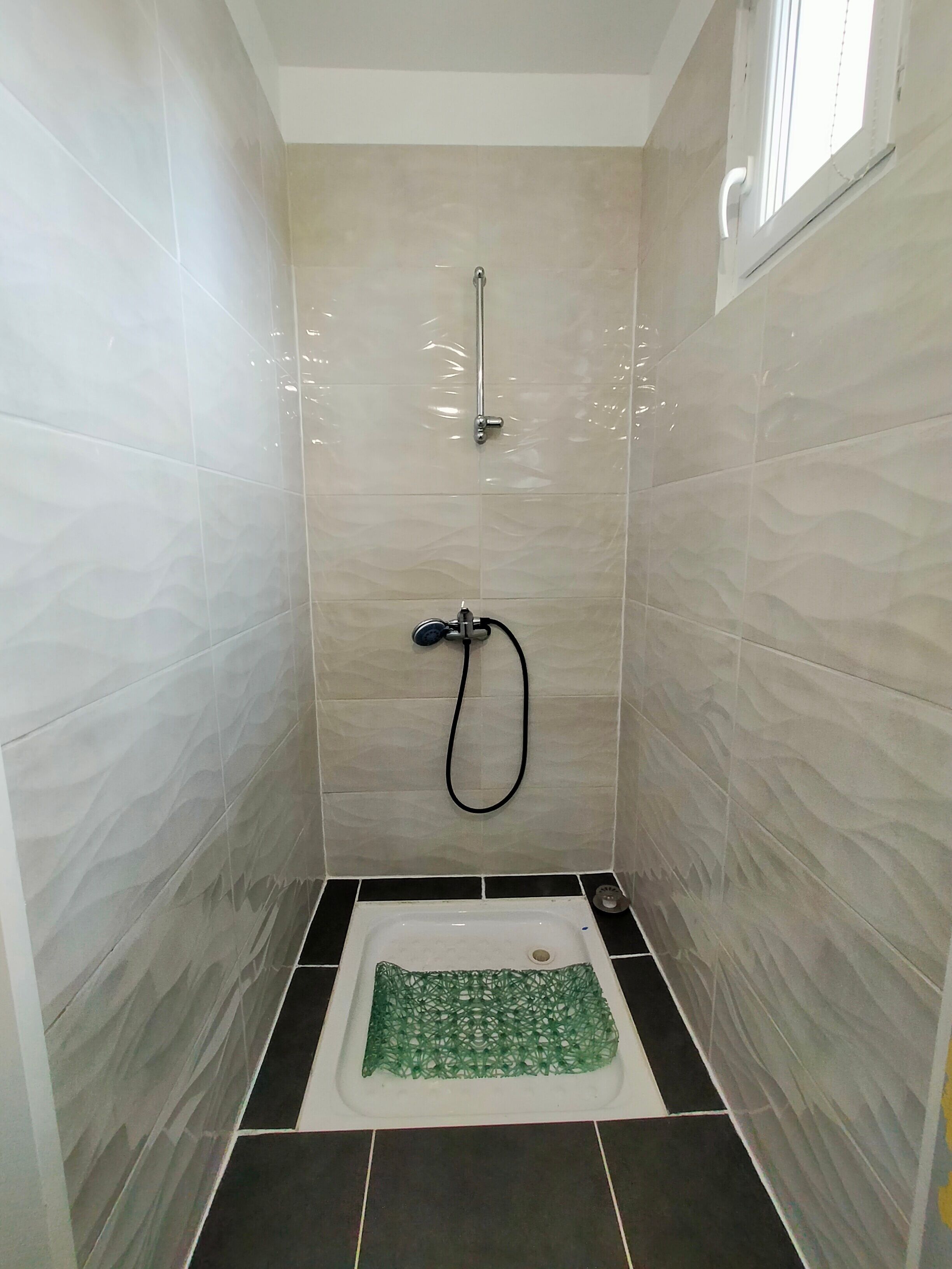 A small, tiled shower room with a handheld showerhead and a handheld hose.