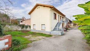 A two-story building with a beige facade, a staircase leading to the upper floor, and a paved driveway.