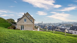 A house with a stone facade, a sloped roof, and a green lawn. - La Tour Vauban - Vue sur le port (Port-en-Bessin-Huppain)