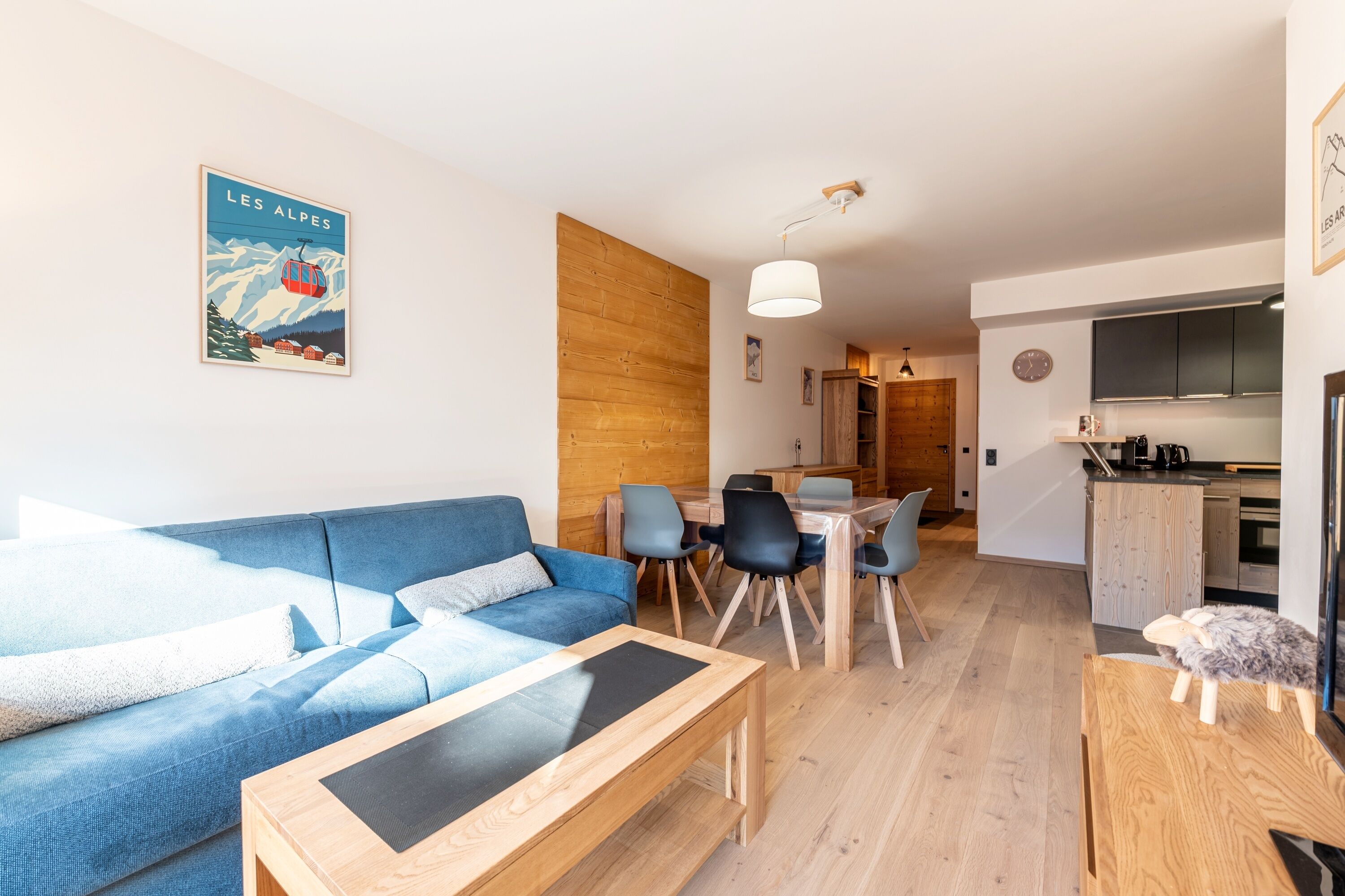 A modern living room with a blue sofa, wooden coffee table, and dining area with chairs and a table.