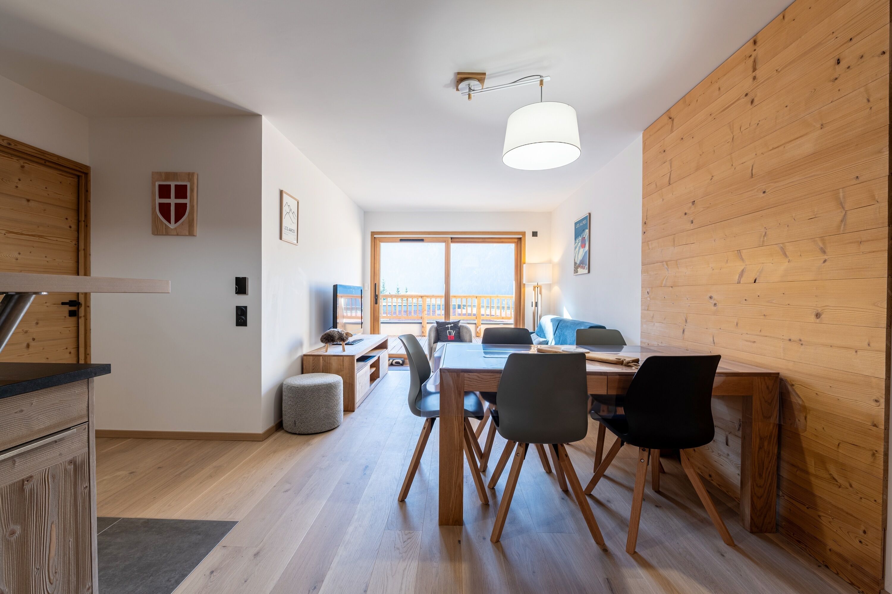 Eine moderne Küche mit Holzausbau, einem Essbereich inklusive Tisch und Stühlen sowie einem großen Fenster, das für natürliches Licht sorgt.