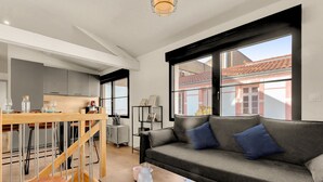 A modern living room with a grey sofa, a wooden dining table, and a kitchen in the background. - Costa Del Sol - Charmant appt pour 2 avec terrasse (Toulouse)
