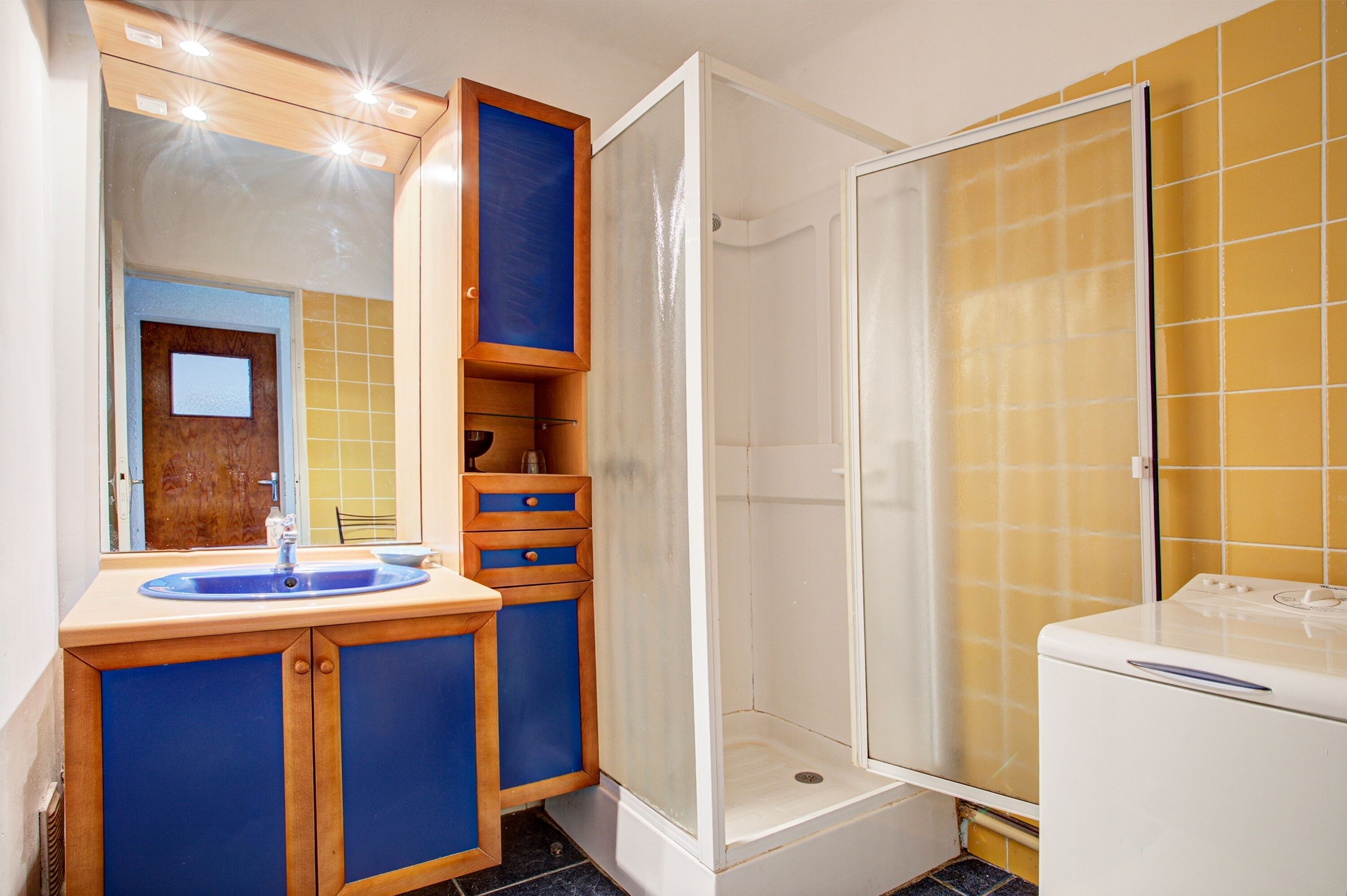 A bathroom with a sink, mirror, cabinet, shower, and a washing machine.