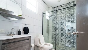 Ein modernes Badezimmer mit Toilette in Weiß, einem Holz-Waschtisch, einer Duschkabine aus Glas und Fliesen mit Muster.