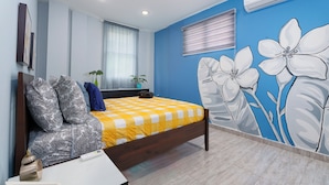 Ein Schlafzimmer mit Bett, Nachttisch, Stuhl, einem Fenster mit Vorhängen und Wandbild.
