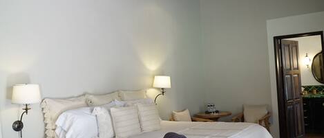 A bedroom with a bed, bedside lamps, a ceiling fan, and a small table with a chair.