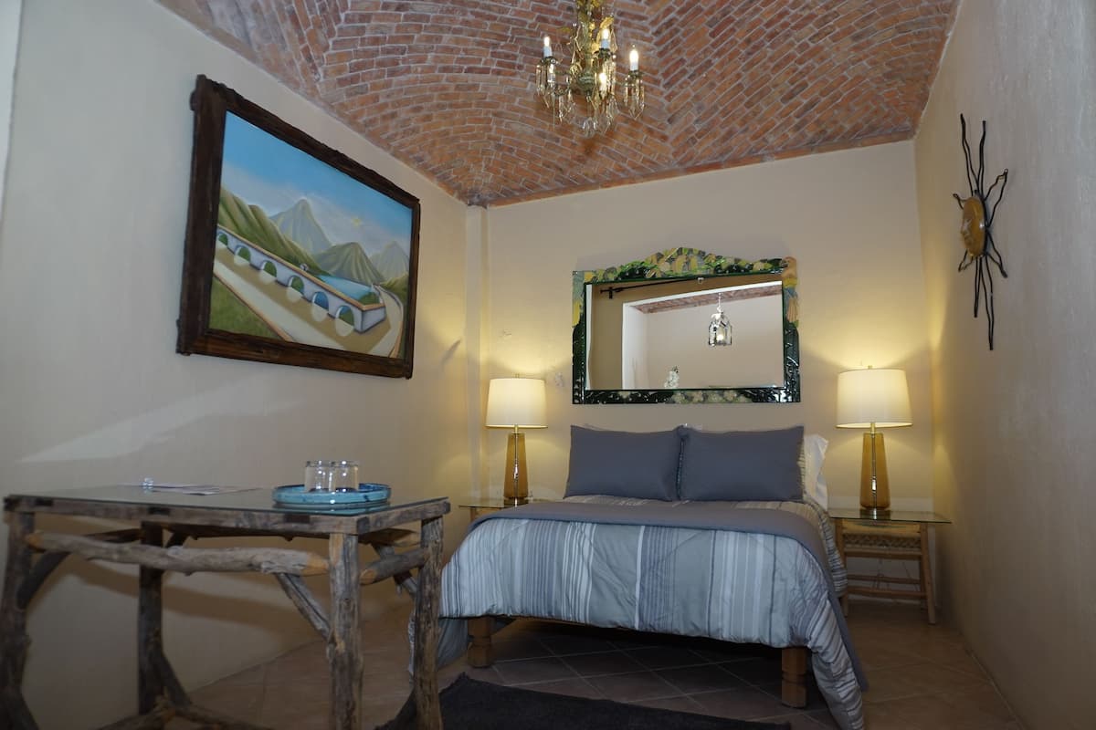 Een slaapkamer met een bed, twee nachtkastjes met lampen, een schilderij aan de muur en een kroonluchter.