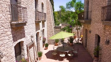 A courtyard with stone buildings, a round table with chairs, and potted plants.