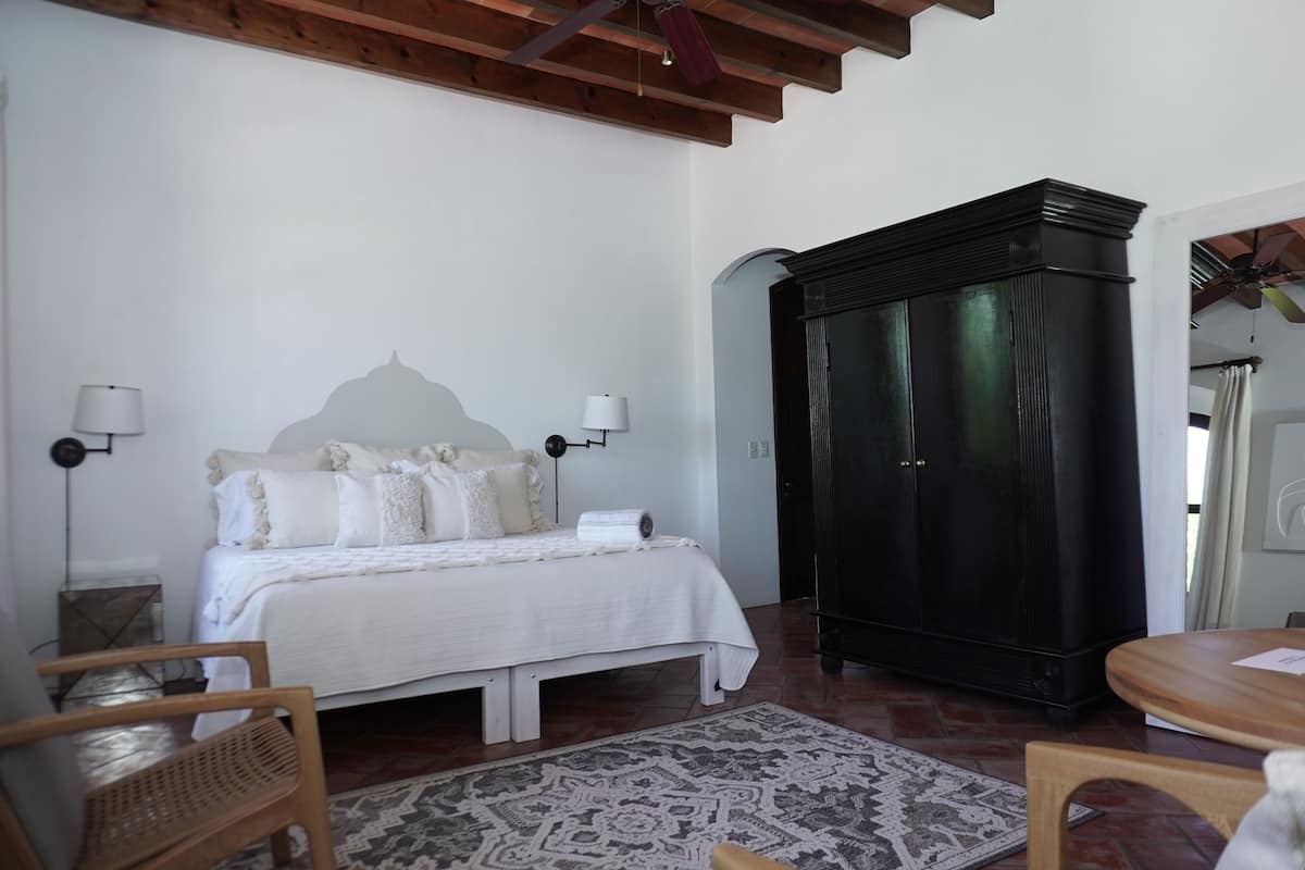 Een slaapkamer met een bed, bedlampen, een houten garderobe, een tapijtgoud en een houten stoel.