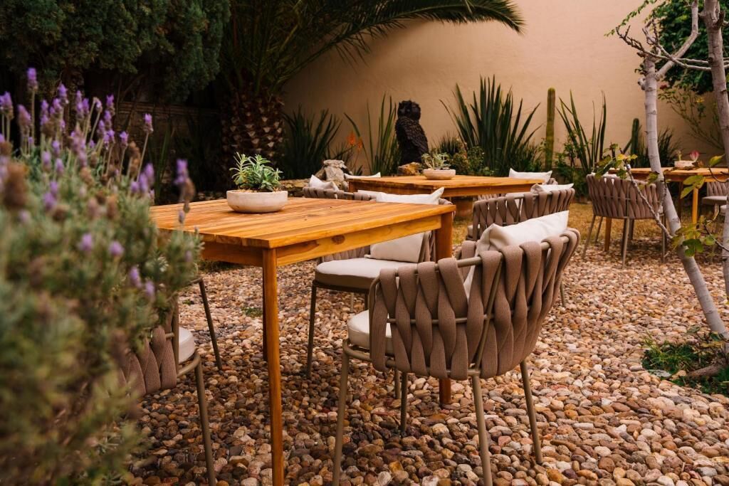 Un espace extérieur aménagé en terrasse, avec des tables en bois et des chaises en osier, entouré de galets et de différentes plantes.