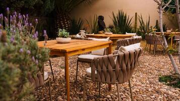 Un espace extérieur aménagé en terrasse, avec des tables en bois et des chaises en osier, entouré de galets et de différentes plantes.