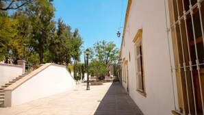 A narrow, sunlit street with a staircase on the left and a building with barred windows on the right. - Hotel Casa Mexicana (Mineral de Pozos)