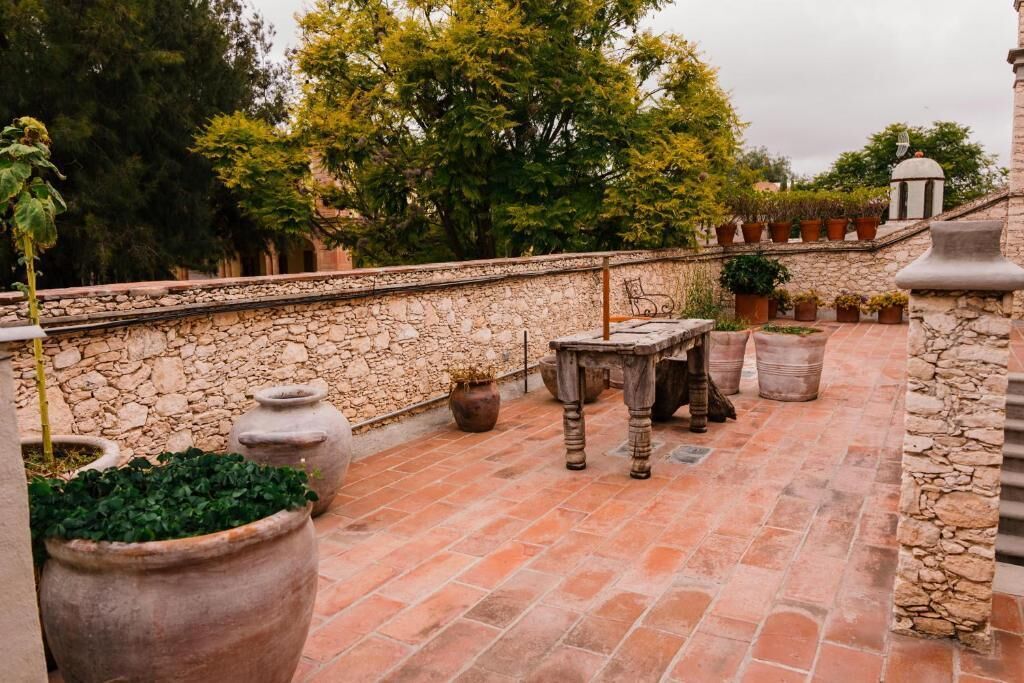 A stone-walled outdoor patio with terracotta tiles, a rustic wooden table, and potted plants.