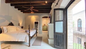 A bedroom with a large bed, a ceiling fan, and a view of a courtyard through an open door. - Hotel Casa Mexicana (Mineral de Pozos)
