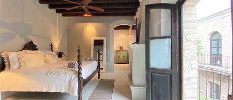 A bedroom with a large bed, a ceiling fan, and a view of a courtyard through an open door.