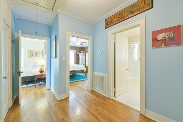 A hallway with wooden flooring, a bed with a white comforter, a nightstand with a lamp, and a ceiling fan. - BEE Inn BRENHAM Holiday Cottage - Premium location walking distance to downtown. (Brenham)