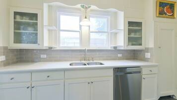 A kitchen with white cabinets, a double sink, a dishwasher, and a window with a decorative ceiling light.